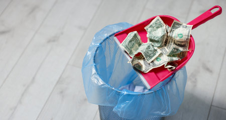 Dollar banknotes, dustpan and trash bin on floor, closeup. Space for textの写真素材