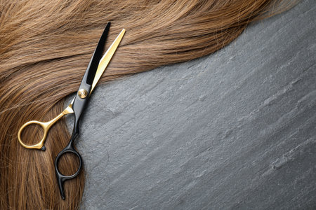 Beautiful hair strands and scissors on gray background, top view. Space for textの写真素材