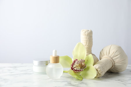 Beautiful spa composition with herbal bags and essential oil on white marble table against light background. Space for textの写真素材