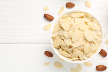 Fresh almond flakes and whole nuts on white wooden table, top view. Space for textの写真素材