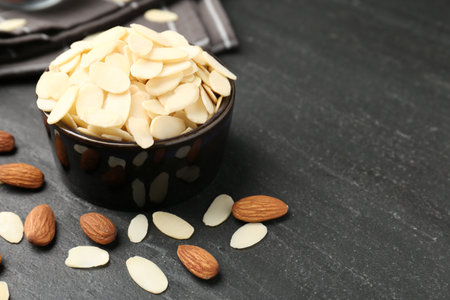 Fresh almond flakes in bowl and whole nuts on gray table, closeup. Space for textの写真素材
