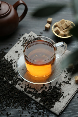 Aromatic black tea in glass cup, dried leaves, brown sugar and teapot on wooden table, closeupの写真素材