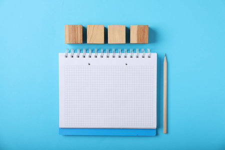 Blank wooden cubes, notebook and pencil on light blue background, flat lay