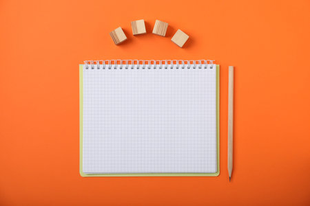 Blank wooden cubes, notebook and pencil on orange background, flat layの写真素材