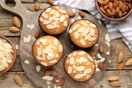 Tasty muffins with almond flakes and nuts on wooden table, flat layの写真素材