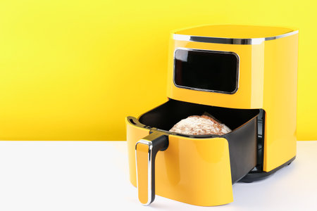 Air fryer with baked bread on white table against yellow background, closeup. Space for textの写真素材