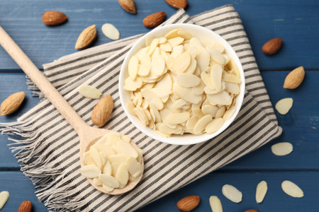 Fresh almond flakes and whole nuts on blue wooden table, flat layの写真素材