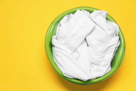Plastic basin with clothes on yellow background, top view. Space for textの写真素材