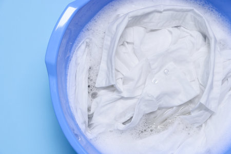Plastic basin with clothes, water and foam on light blue background, top viewの写真素材