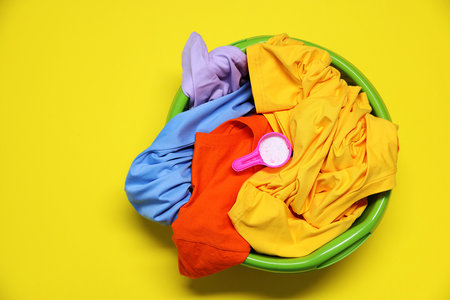 Plastic basin with clothes and washing powder on yellow background, top viewの写真素材
