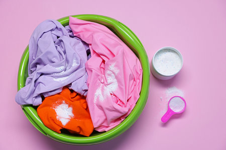 Plastic basin with clothes and washing powder on pink background, top viewの写真素材