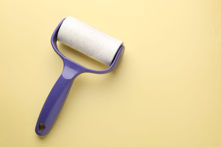 Lint roller with used sticky tape on yellow background, top view. Space for text