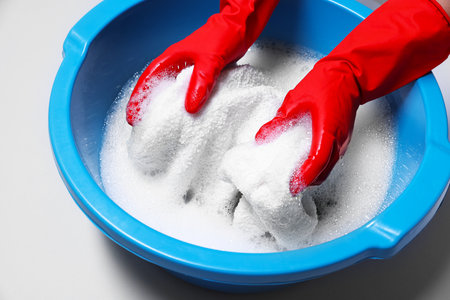 Woman washing clothes in plastic basin on light gray background, closeupの写真素材