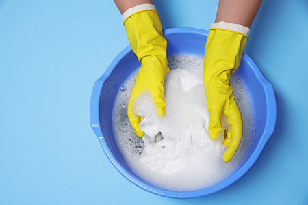 Woman washing clothes in plastic basin on light blue background, top viewの写真素材