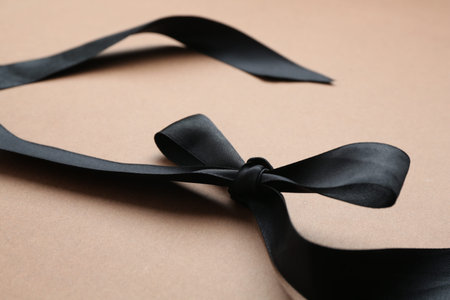 Beautiful black ribbon with bow on light brown background, closeup