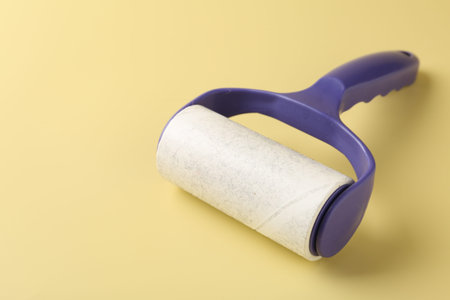 Lint roller with used sticky tape on yellow background, closeup. Space for text