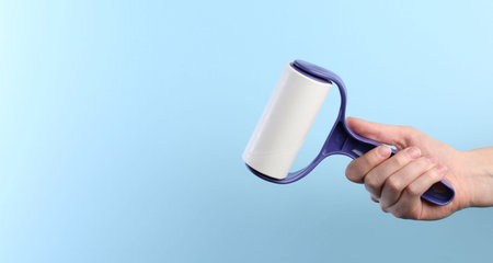 Woman with lint roller on light blue background, closeup. Space for textの写真素材