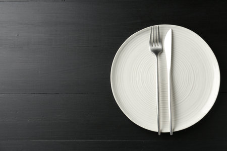 Clean ceramic plate and cutlery on black wooden table, top view. Space for textの写真素材