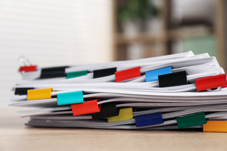 Stack of documents with binder clips on wooden table indoors, closeup