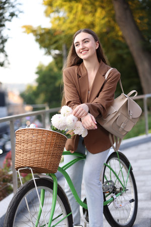 Woman riding bicycle with flowers in basket on city streetの写真素材