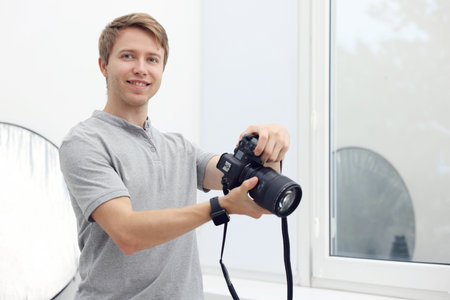 Professional photographer with camera near window in studio, space for textの写真素材