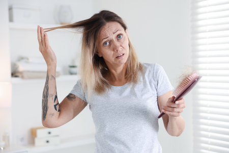 Worried woman with hair loss problem holding brush at homeの写真素材