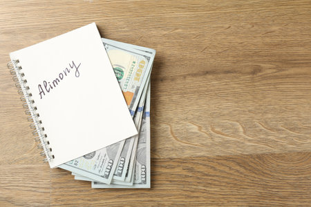 Notebook with word alimony and money on wooden table, top view. Space for textの写真素材