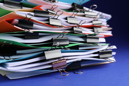 Many folders with documents and binder clips on blue background, closeup