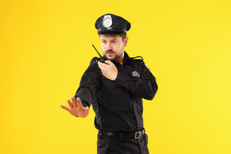 Policeman in uniform with walkie talkie showing stop gesture on yellow backgroundの写真素材