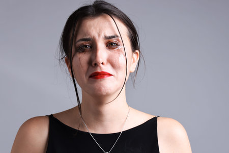 Woman with smeared mascara crying on gray background