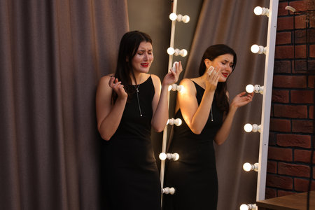 Emotional woman with smeared mascara in dress crying near mirror indoorsの写真素材