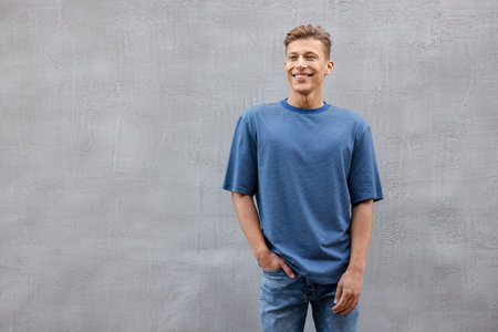 Young man wearing blank blue t-shirt near gray wall. Mockup for designの写真素材