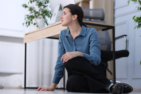 Young businesswoman on floor near desk in office, space for textの写真素材