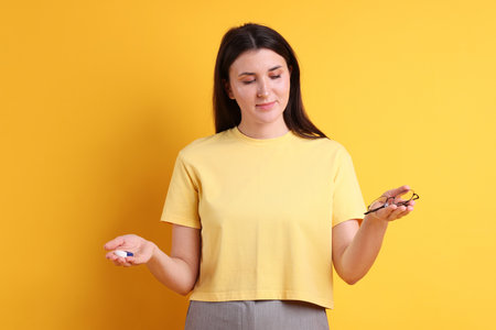 Young woman choosing between glasses and contact lenses on orange backgroundの写真素材