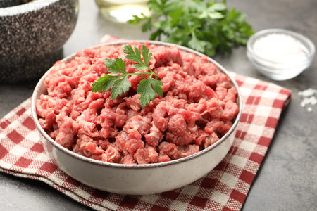 Raw minced meat with parsley and spices on gray table, closeup