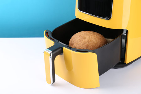 Air fryer with baked bread on white table against light blue background, closeup. Space for text