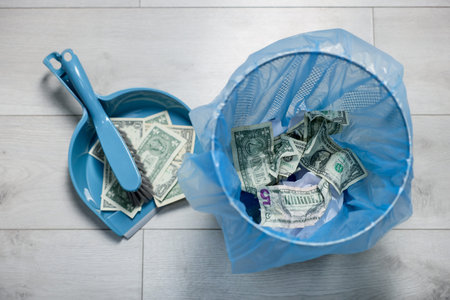 Dollar banknotes in trash bin, dustpan and broom on floor, flat layの写真素材