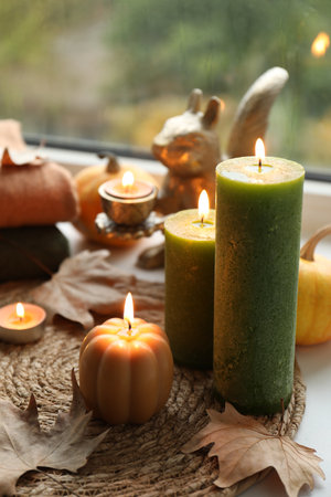 Burning candles and dry leaves on windowsill on rainy day. Autumn atmosphereの写真素材