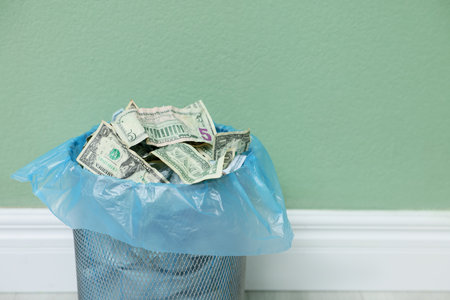 Dollar banknotes in trash bin near green wall indoors, closeup. Space for textの写真素材