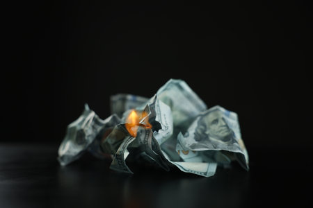 Burning dollar banknotes on black table against dark backgroundの写真素材