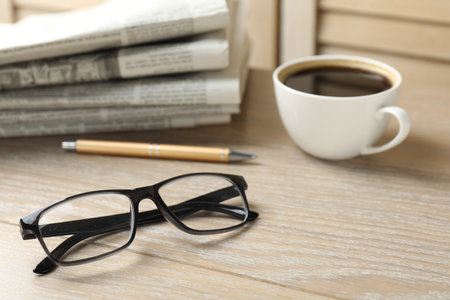 Stack of newspapers, coffee, pen and glasses on wooden table, closeupの写真素材