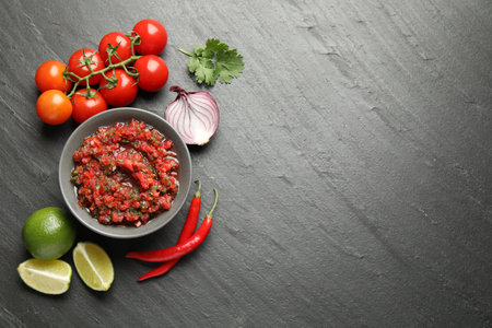 Delicious salsa sauce in bowl and ingredients on dark grey table, flat lay. Space for textの写真素材