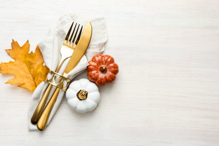 Beautiful table setting. Cutlery with napkin and autumn decor on white wooden background, top view. Space for textの写真素材