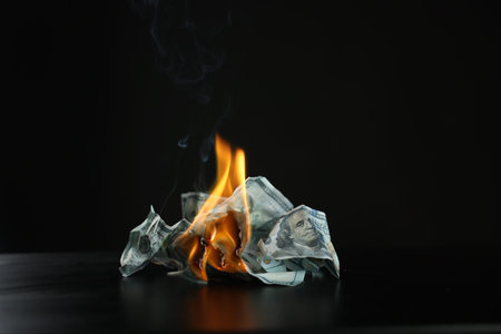 Burning dollar banknotes on black table against dark backgroundの写真素材
