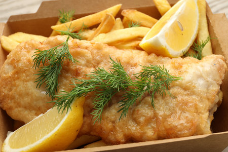 British Traditional Fish and chips with lemon in paper box on table, closeup
