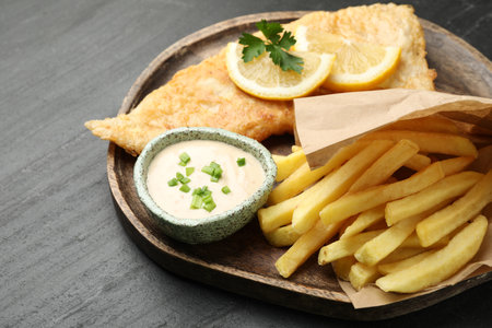 British Traditional Fish and chips with sauce, lemon and parsley on dark textured table, closeupの写真素材