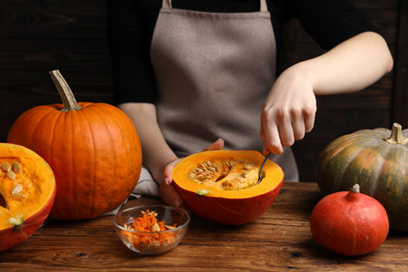 Woman removing seeds from raw pumpkin at wooden table, closeupの写真素材