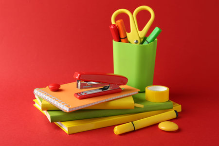 Stapler and other stationery on red background. Space for text