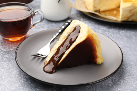 Piece of delicious Basque cheesecake with chocolate sauce and tea on grey table, closeupの写真素材