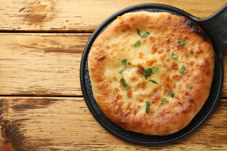 Delicious Megrelian khachapuri with parsley on wooden table, top view. Space for textの写真素材